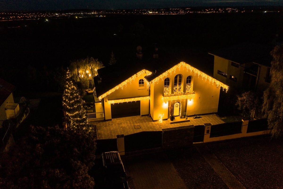 Wohnhaus von oben mit Lichterkette am Dach und beleuchtetem Baum im Vorgarten bei Nacht