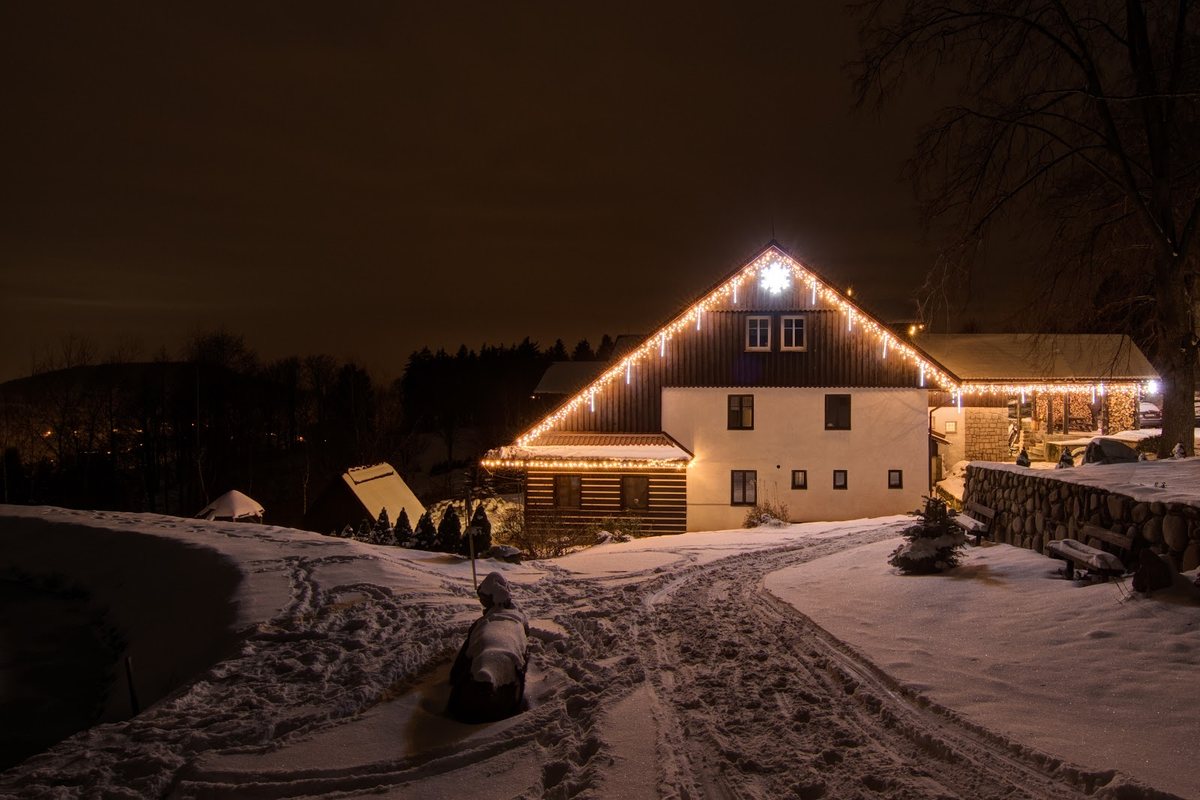 Wohnhaus bei Nacht mit LED-Lichterkette entlang First und Traufe, Schnee im Vorgarten